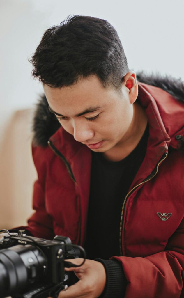 Focused Asian man in red warm jacket with video camera